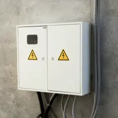 Biała skrzynka elektryczna z żółtymi symbolami ostrzegawczymi. Kto odpowiada za rury przed licznikiem? Instalacja elektryczna.