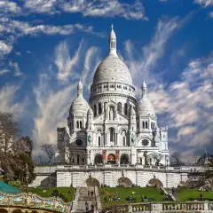 Bazylika Sacré-Cœur na wzgórzu Montmartre w Paryżu, z karuzelą w tle i dramatycznym niebem.