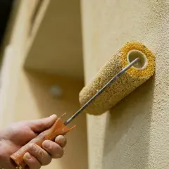 En hand målar en texturerad vägg med en rulle. Det ser ut som att man målar puts för att ge den nytt liv.
