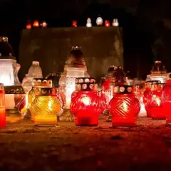 Płonące znicze na cmentarzu. Wiele świec w szklanych pojemnikach, niektóre czerwone, inne żółte, tworzą ciepłe światło. To symbol pamięci i zadumy, często towarzyszy im szczególna pogoda na pogrzebie, co oznacza głęboką refleksję.