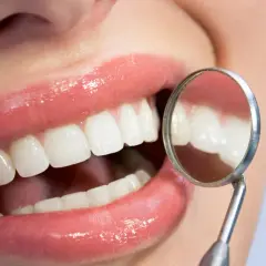 Uśmiech z lśniącymi zębami, badany lusterkiem dentystycznym. Zdrowe dziąsła to podstawa, by uniknąć problemów jak szkorbut.