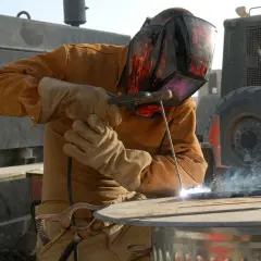Spawacz w masce z płomieniami używa elektrody rutylowej do łączenia metalowych elementów.