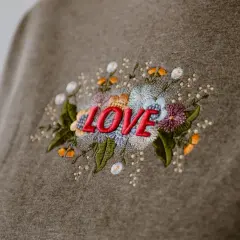 Besticktes Sweatshirt mit dem Wort "LOVE" umgeben von bunten Blumen. Zeigt, was man besticken kann.