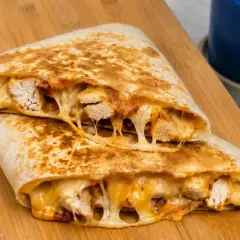 Pyszna quesadilla z kurczakiem, z ciągnącym się serem i kawałkami soczystego mięsa, podana na drewnianej desce.