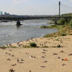 Słoneczna poniatówka nad Wisłą. Ludzie opalają się na piaszczystej plaży, w tle most i panorama Warszawy.