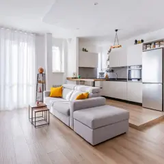 Un ampio open space moderno con divano grigio, cucina a vista e pavimento in legno chiaro.
