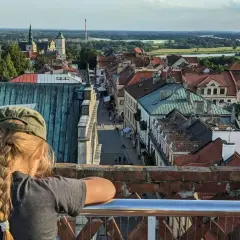 Widok z góry na Sandomierz, z dziewczynką w czapce na pierwszym planie. W oddali widać Wisłę i charakterystyczną Brama Opatowska.