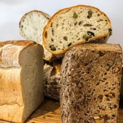 Różnorodne pieczywo, w tym bochenek z ziarnami i kromka z oliwkami. Czy chleb żytni ma gluten? Tak, większość chlebów, w tym żytni, zawiera gluten.