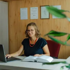 Uśmiechnięta prawniczka przy biurku z laptopem i książką. Dowiedz się, ile kosztuje sprawa o zasiedzenie u adwokata.