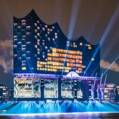 Elbphilharmonie, konserthus Hamburg, badar i ljus och strålkastare över vattnet en mörk kväll.
