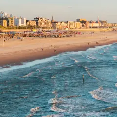 Ein sonniger Tag an der Nordsee Holland. Wellen brechen am Strand, im Hintergrund die Stadtkulisse mit Hotels und Strandpavillons.