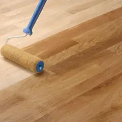 Un rouleau applique un fondur pour bois sur un parquet clair, le transformant en un bois plus foncé et chaleureux.