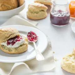 Ein Scone mit Clotted Cream und Marmelade, daneben eine Tasse Kaffee und weitere Scones.