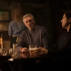 Besetzung von Damaged: Vincent Cassel und Reda Kateb sitzen in einer dunklen Bar bei Bier.