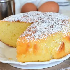 Una soffice torta al limone, spolverata di zucchero a velo, pronta per essere gustata. Ingredienti freschi come uova e limone sullo sfondo.
