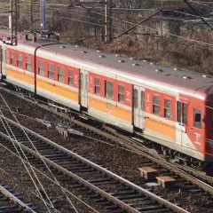 Czerwono-pomarańczowy pociąg elektryczny EN57 na torach.