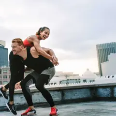 Parać na dachu, kobieta na plecach mężczyzny, oboje uśmiechnięci, w sportowych strojach. Idealny multisport dla osoby towarzyszącej.