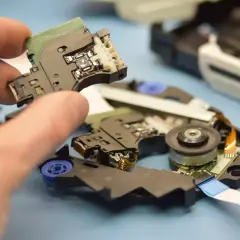 Dłoń trzyma element z soczewką lasera, część mechanizmu odtwarzacza DVD. Diak jest kluczowy dla odczytu danych.