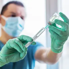 Medyk w zielonych rękawiczkach pobiera płyn do strzykawki, przygotowując szczepionkę na tężec.