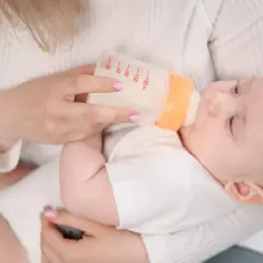 Mama karmi dziecko butelką z mlekiem. Na butelce widać miarkę, jak przy wycofanym mleku Bebilon.