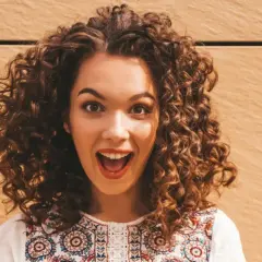 Mujer con cabello apelmazado y rizado, con una expresión de sorpresa y alegría.