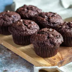 Muffins med chokladbitar, saftiga och mörka, ligger uppradade på en träbricka. Perfekta för fikat!