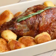 Gigot d'agneau rôti, garni de romarin, entouré de pommes de terre au four dorées et croustillantes. Un plat savoureux prêt à être dégusté.
