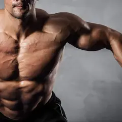 Uomo muscoloso con addominali scolpiti, che si allena con cavi. Ideale per chi cerca recupero e crescita muscolare con aminoacidi dopo allenamento.