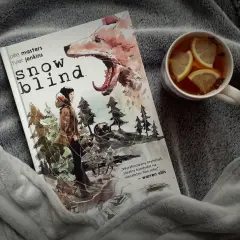 Okładka komiksu "Snow Blind" z wilkiem i postacią w lesie. Obok kubek z herbatą i cytryną. Idealny thriller na zimowe wieczory.