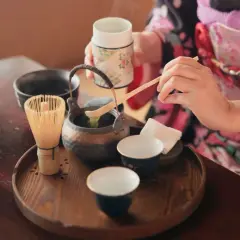 Eine Person in einem Kimono bereitet eine traditionelle matcha zeremonie vor. Ein Chasen (Bambusbesen) und eine Schale mit Matcha-Pulver sind auf einem Holzteller arrangiert.