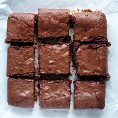 Nio saftiga bitar av glutenfri brownie ligger uppskurna på bakplåtspapper.
