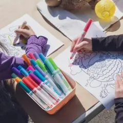 Zwei Kinder malen Osterbilder. Ein bunter Kasten mit Stiften liegt bereit, wie ein Laufzettel für die Grundschule.