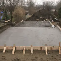 Plac budowy z wylana płytą betonową, przygotowywaną pod fundamenty. Widać zbrojenie i szalunki, wskazujące na różne klasy ekspozycji betonu.