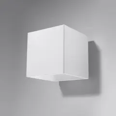 Minimalistyczna lampa kostka w kolorze białym, zamontowana na szarej ścianie. Rzuca subtelny cień.