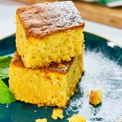 Dos porciones de bizcocho de calabaza apiladas, espolvoreadas con azúcar glas, junto a hojas de menta fresca en un plato azul.