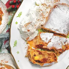 Delizioso strudel di mele con pasta sfoglia, cosparso di zucchero a velo e servito con panna montata e cannella.