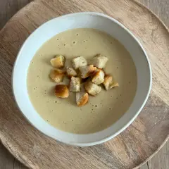 Aksamitna zupa cebulowa krem, udekorowana chrupiącymi grzankami, podana na drewnianej desce.