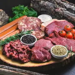 Mięsa, kiełbaski, pomidorki i przyprawy na drewnianej desce. Zastanawiasz się, ile cukru do solanki na wędliny?