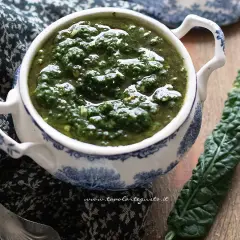 Pesto di cavolo nero in una ciotola decorata, accanto a una foglia fresca. Un condimento sano e saporito.