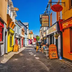Färgglad gränd med butiker och caféer. En skylt för "Spögler's Continental Cakes Coffee Shop" syns tydligt, liksom en barberare. Kanske en trevlig plats att besöka efter en tur i Dublin.