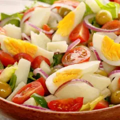Deliciosa ensalada de patata con huevo duro, tomate, cebolla morada y aceitunas verdes en un cuenco de madera.