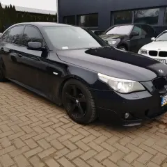 Ciemnogranatowe BMW E60 535d na czarnych felgach, zaparkowane na kostce brukowej przed budynkiem.