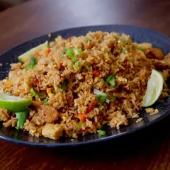 En tallrik med khao pad, en smakrik thailändsk stekt risrätt med kyckling, grönsaker och limeklyftor.