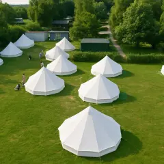 Malowniczy **pole glampingowe** z białymi namiotami na zielonej trawie, otoczone drzewami.