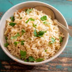 Un tazón de arroz integral cocido con perejil fresco y una cuchara.
