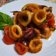 Anelli di calamari croccanti e pomodorini cotti nella friggitrice ad aria, guarniti con una foglia di basilico.