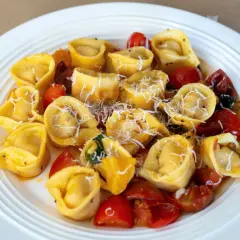 Domowe tortellini z mięsem, pomidorkami i parmezanem na białym talerzu.