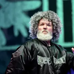 Fred Durst z Limp Bizkit na koncercie, z charakterystyczną fryzurą i brodą, w czarnej kurtce z logo zespołu.