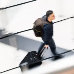 Mężczyzna z plecakiem i walizką na kółkach w ruchu.