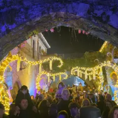 Gente disfrutando del mercado navideño en Cartes, con luces brillantes y ambiente festivo bajo un arco de piedra.